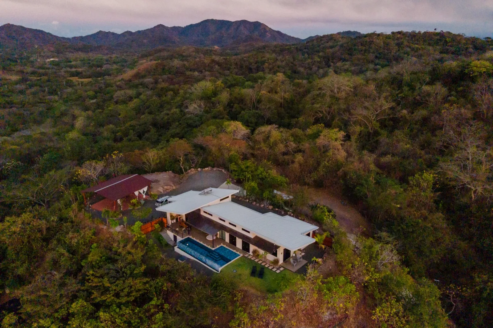 Aerial view of Toltec Estate on its private hilltop, surrounded by jungle canopy with mountains behind