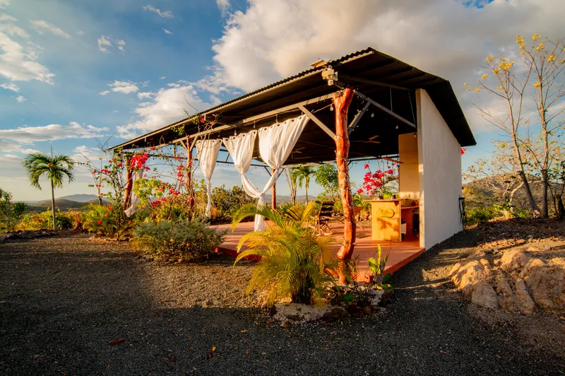 The open-air yoga studio at golden hour, white curtains and bougainvillea framing the view
